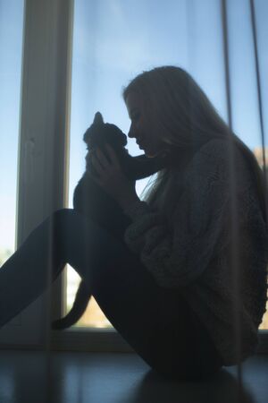 The silhouette of a girl with loose hair and a black kitten on the windowの写真素材