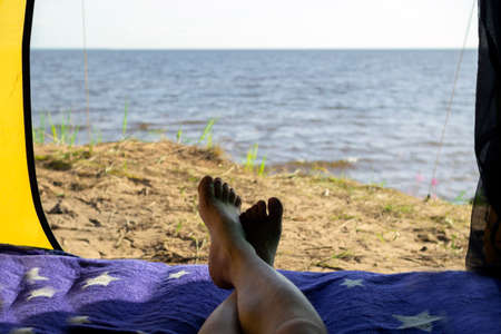Camping man lying in a tent close-up of his feet . Relaxing on the beach.の写真素材