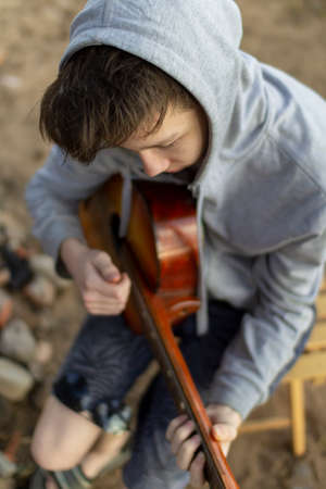 A teenager plays a guitar while sitting on the shore of a lake.の写真素材