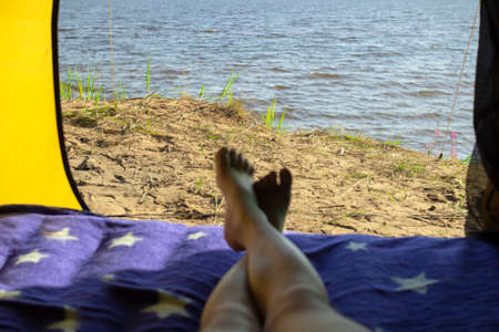 Camping man lying in a tent close-up of his feet . Relaxing on the beach.の写真素材