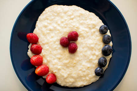 Oatmeal porridge with berries, in a blue plate. Healthy breakfast.