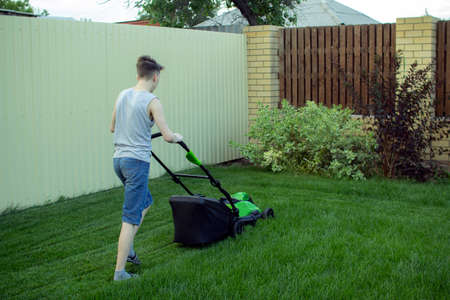 A teenager mows the lawn with a lawn mower.