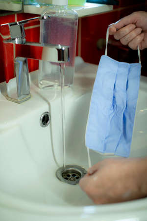Washing a medical mask in the sink. Cotton reusable medical mask for protection from Covid-19.の写真素材