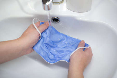 Washing a medical mask in the sink. Cotton reusable medical mask for protection from Covid-19.の写真素材