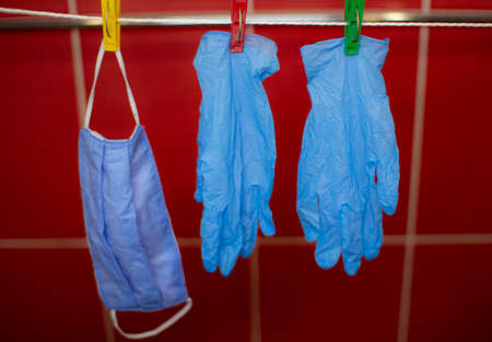 Medical masks and gloves hang on a clothesline on plastic clothespins. Red background. Protection from coronavirus.の写真素材
