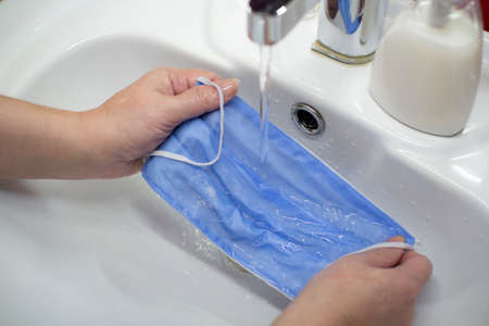 Washing a medical mask in the sink. Cotton reusable medical mask for protection from Covid-19.の写真素材