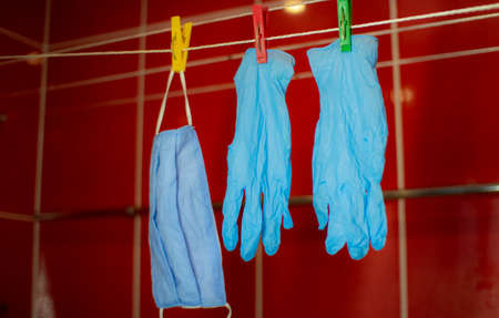 Medical masks and gloves hang on a clothesline on plastic clothespins. Red background. Protection from coronavirus.の写真素材