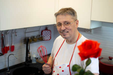 A man in an apron cooks in the kitchen and meets his girlfriend with a rose in her hands.の写真素材