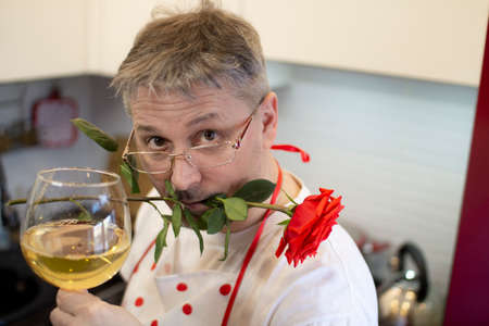 A man in an apron cooks in the kitchen and meets his girlfriend, offering a rose and wine.の写真素材