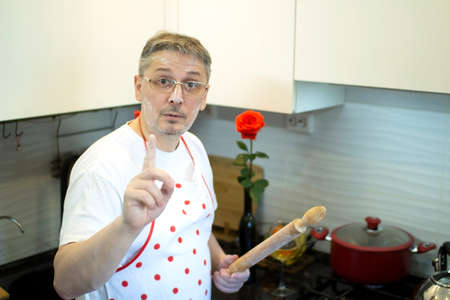 A man in an apron in the kitchen with a rolling pin in her hands.の写真素材