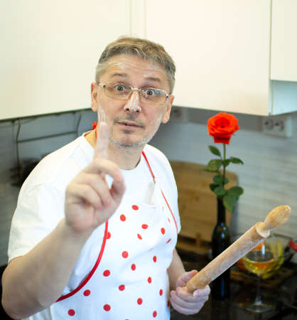 A man in an apron in the kitchen with a rolling pin in her hands.の写真素材