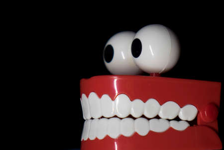 A smiling toy prosthesis, with white teeth and large eyes isolated against a black background.の写真素材
