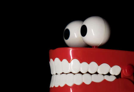 A smiling toy prosthesis, with white teeth and large eyes isolated against a black background.の写真素材