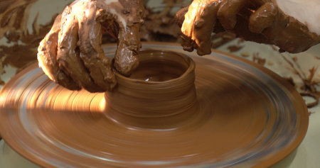 The potters wheel. A close-up of the hands of a craftsman skillfully working with clay on a potters wheel, giving it the shape of a clay productの写真素材