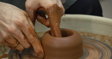 The potters wheel. A close-up of the hands of a craftsman skillfully working with clay on a potters wheel, giving it the shape of a clay productの写真素材
