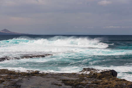 Turbulent ocean waves with white foam beat coastal stones