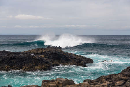 Turbulent ocean waves with white foam beat coastal stones