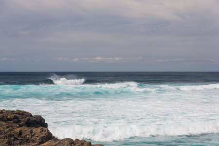 Turbulent ocean waves with white foam beat coastal stones