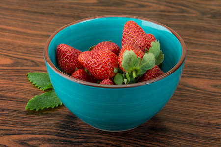 Fresh ripe strawberries in the bowl on wooden backgroundの写真素材