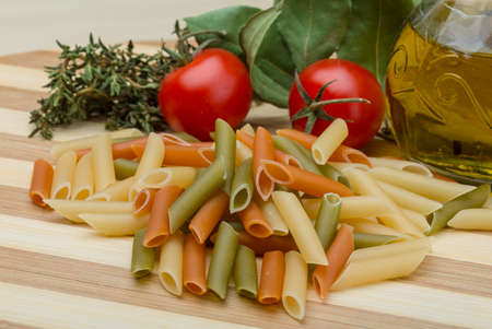 Raw penne pasta various color with herbs on the wood backbroundの写真素材