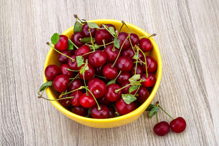 Cherry in the bowl with leaves on wood backgroundの写真素材