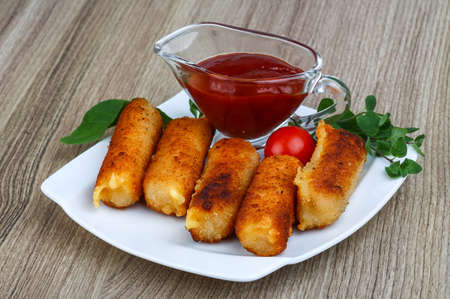Roasted cheese sticks with herbs and sauce on the wood background
