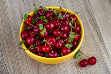 Cherry in the bowl with leaves on wood backgroundの写真素材