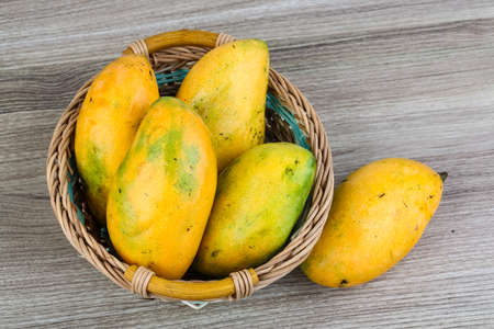 Ripe yellow mangoes in the basket on wood backgroundの写真素材