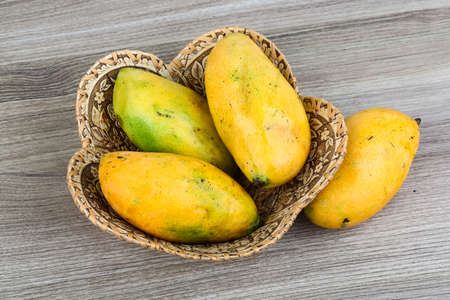 Ripe yellow mango in the basket on wood backgroundの写真素材
