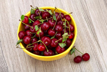 Cherry in the bowl with leaves on wood backgroundの写真素材
