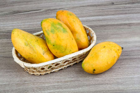 Ripe yellow mango in the basket on wood backgroundの写真素材