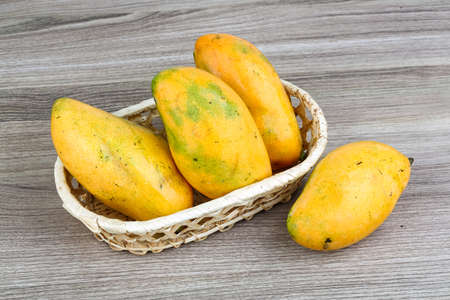 Ripe yellow mango in the basket on wood backgroundの写真素材