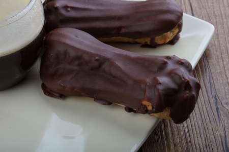 Eclairs with chocolate with coffee on wood bacground