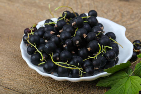 Black currants heap with leaves on wood background