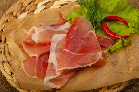 Ham serrano with salad leaves on wood background