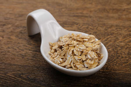 Raw oatmeal heap in the bowl over wooden background