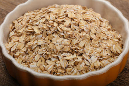 Raw oatmeal heap in the bowl over wooden backgroundの写真素材