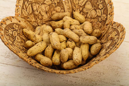 Unpeeled peanuts heap in the basket over wooden baclground