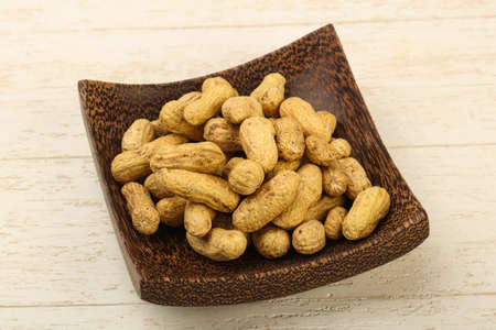 Unpeeled peanuts heap in the basket over wooden background