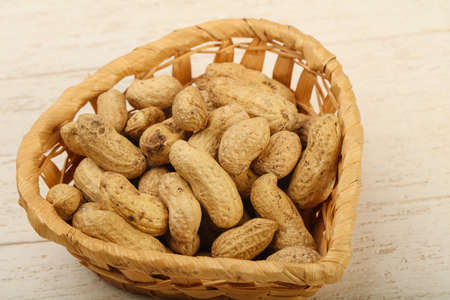 Unpeeled peanuts heap in the basket over wooden baclgroundの写真素材