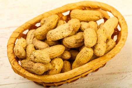 Unpeeled peanuts heap in the basket over wooden baclground