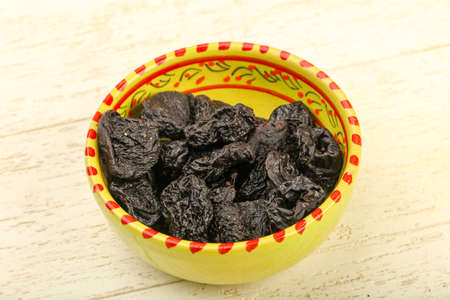 Dried plums heap in the bowl over wooden backgroundの写真素材