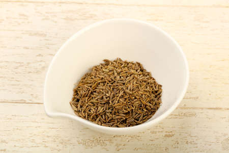 Cumin seeds heap in the bowl over wooden background