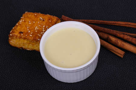 Condenced milk in the bowl with sinnamon sticks and pastryの写真素材