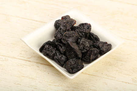 Dried plums heap in the bowl over wooden backgroundの写真素材