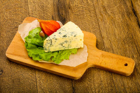 Blue cheese with salad leaves over the wooden background