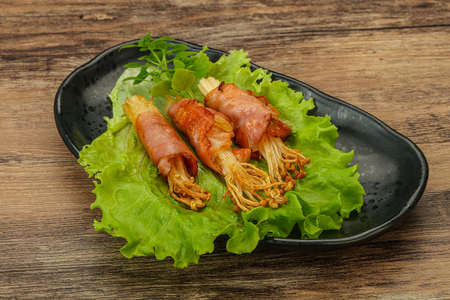 Roasted enoki mushrooms with bacon served basil leavesの写真素材