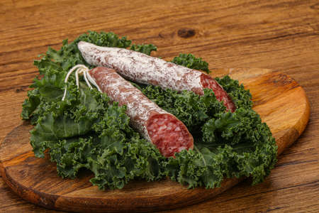 Spanish Fuet sausage with salad leaves over wooden backgroundの写真素材