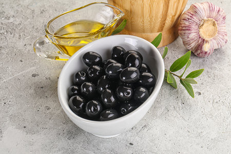 Black olives in the bowl with oil and branchの写真素材