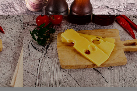 Maasdam cheese piece with slices over board